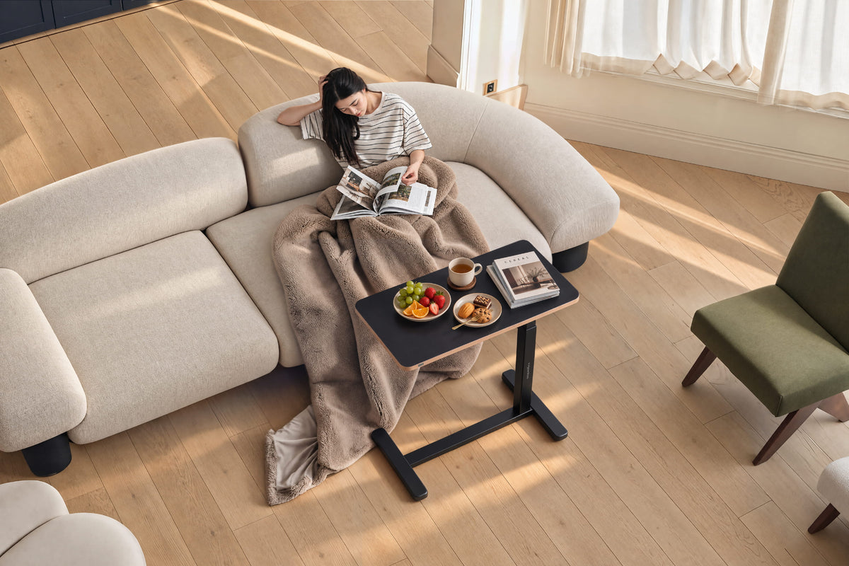 Bàn nâng hạ side table HyperWork Nomad màu đen đặt cạnh sofa, phục vụ nhu cầu đọc sách và thư giãn tại nhà.