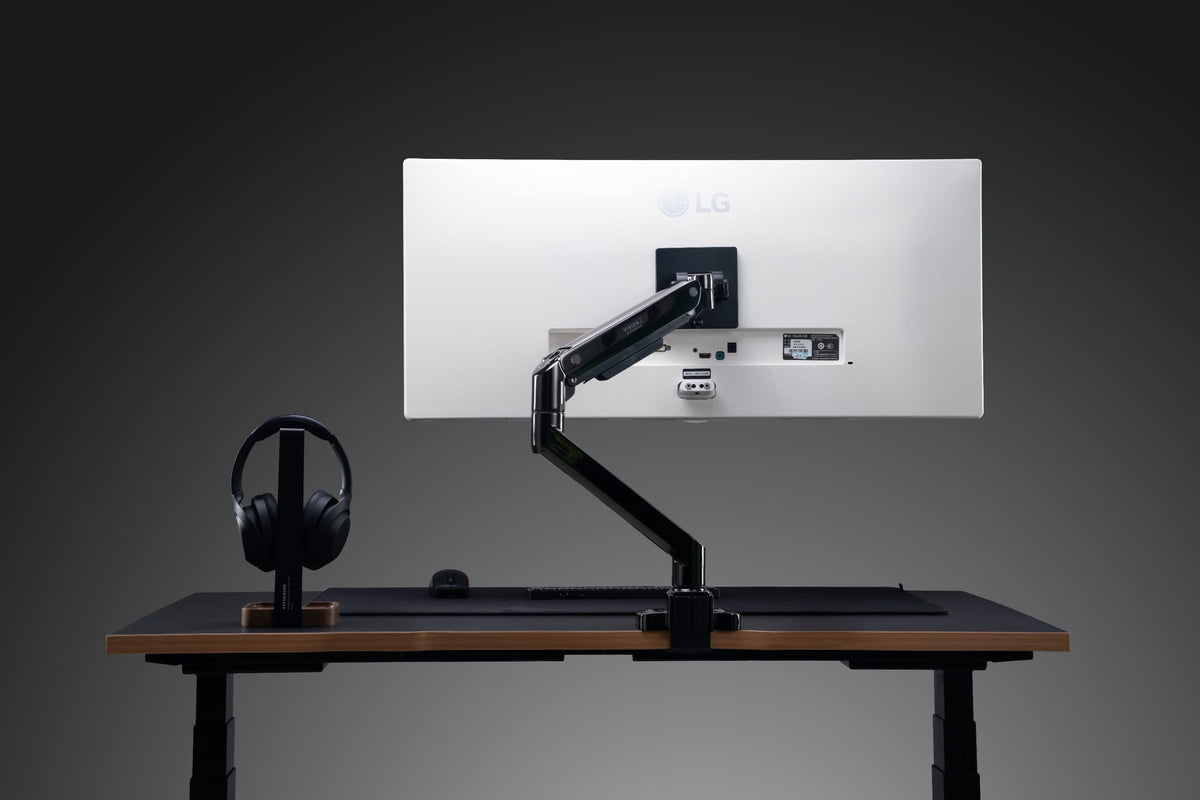 Arm màn hình màu đen gắn màn hình LG trên bàn nâng hạ, tạo góc setup máy tính gọn gàng và hiện đại.
